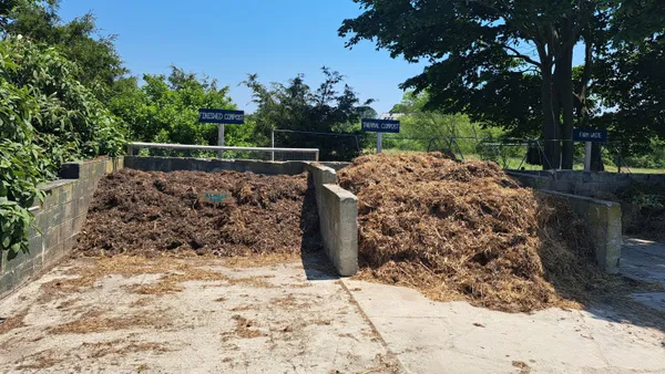 Two piles of brown material, labeled "Finished Compost" and "Almost Done!" are separated by cinderblocks on a concrete pad outside.