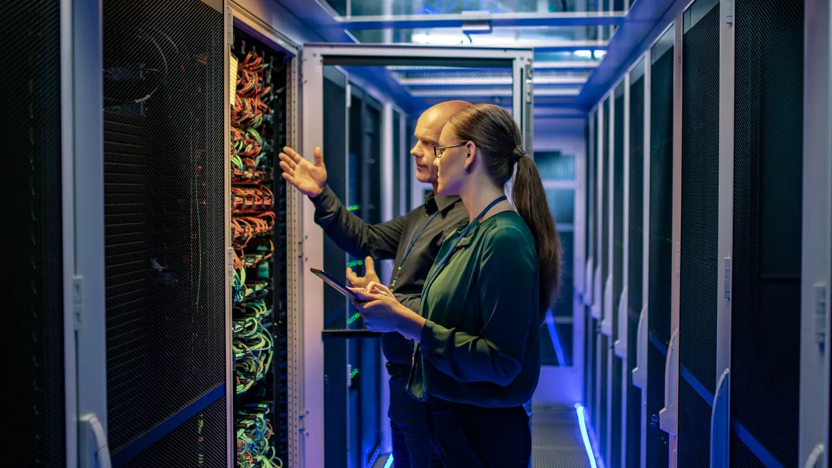 Side view of a man and a woman talking about a server in a data center while looking at it's network connection cables