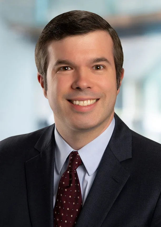 Man with dark hair and brown eyes in a dark suit.