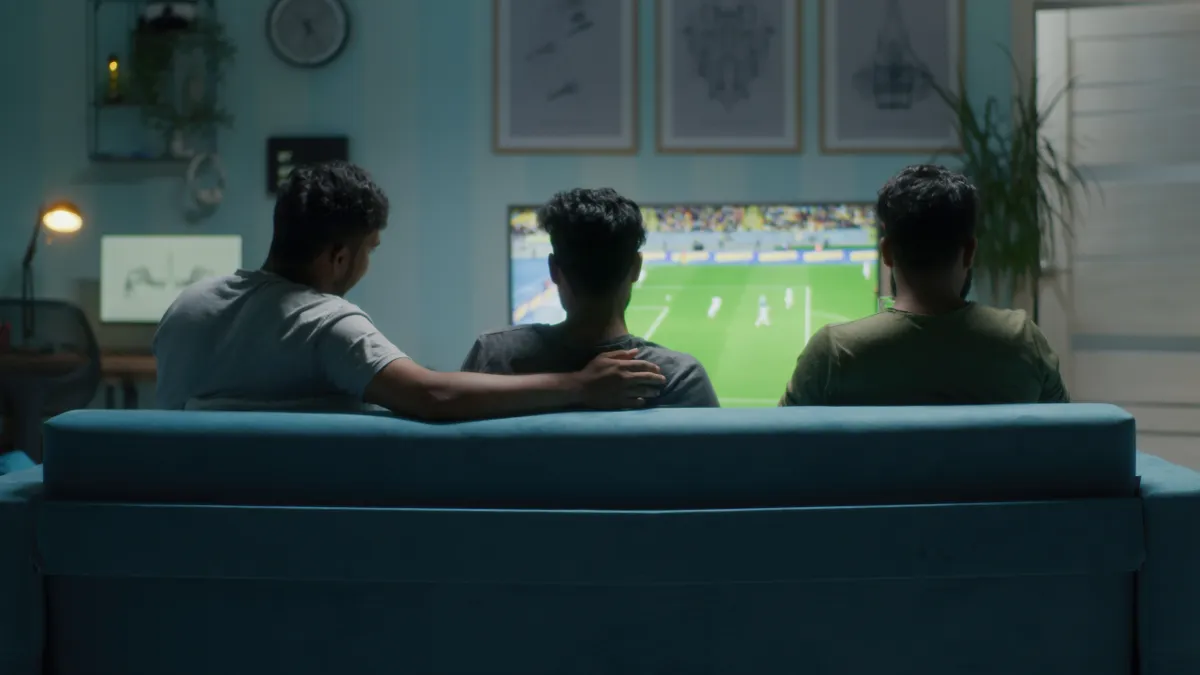 Three people sitting on a couch watching a soccer game on TV.