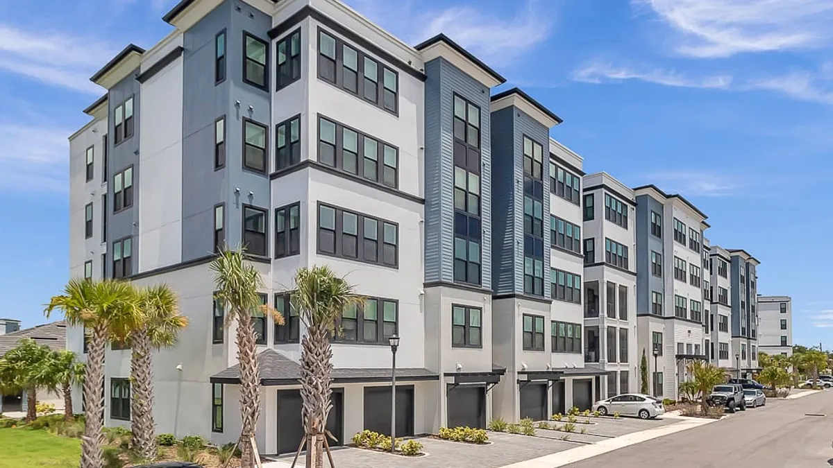 Five-story white apartments surrounded by palm tress and cars