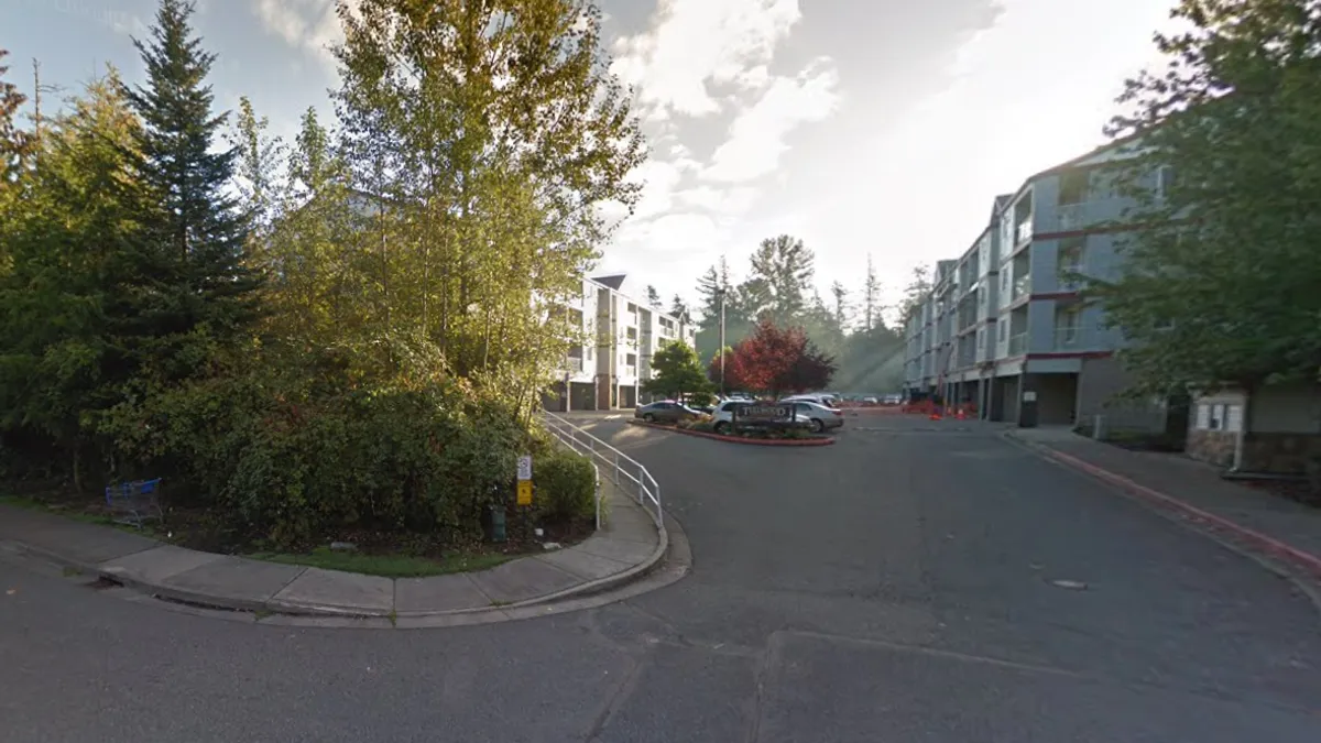 The entrance to an apartment property by the road. Heavy tree cover is located on either side.