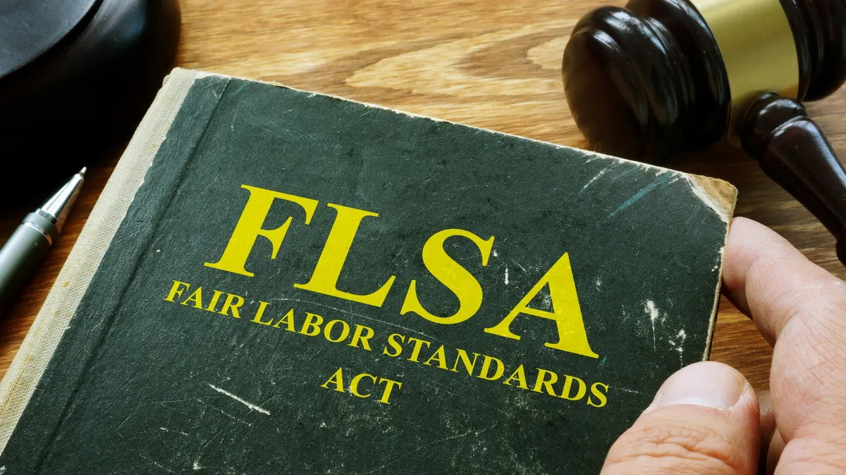 Person holds forest green, worn FLSA fair labor standards act book with a dark brown shiny gavel next to it.