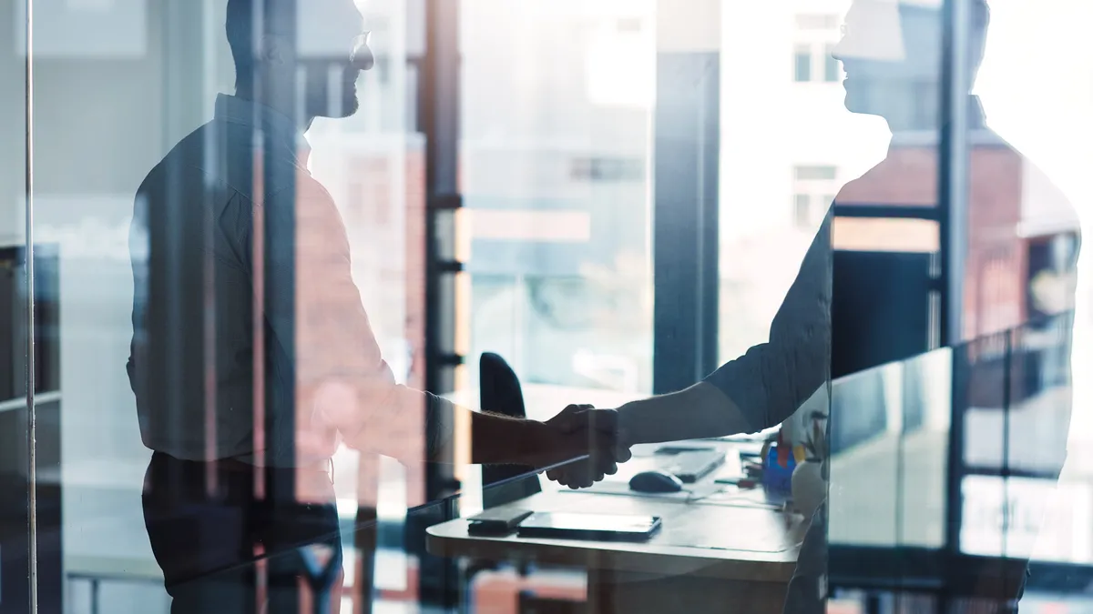 two business people shaking hands through a glass window.