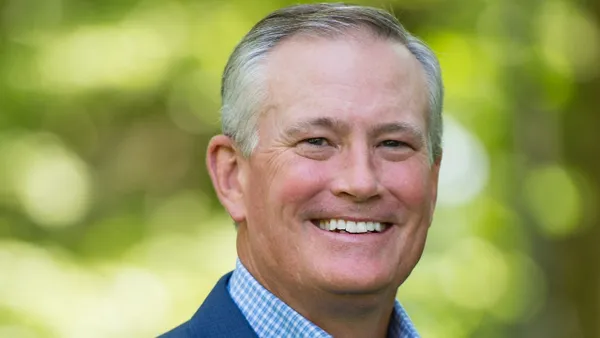 Brian Blaser is smiling in a headshot with a blurred deep green background.