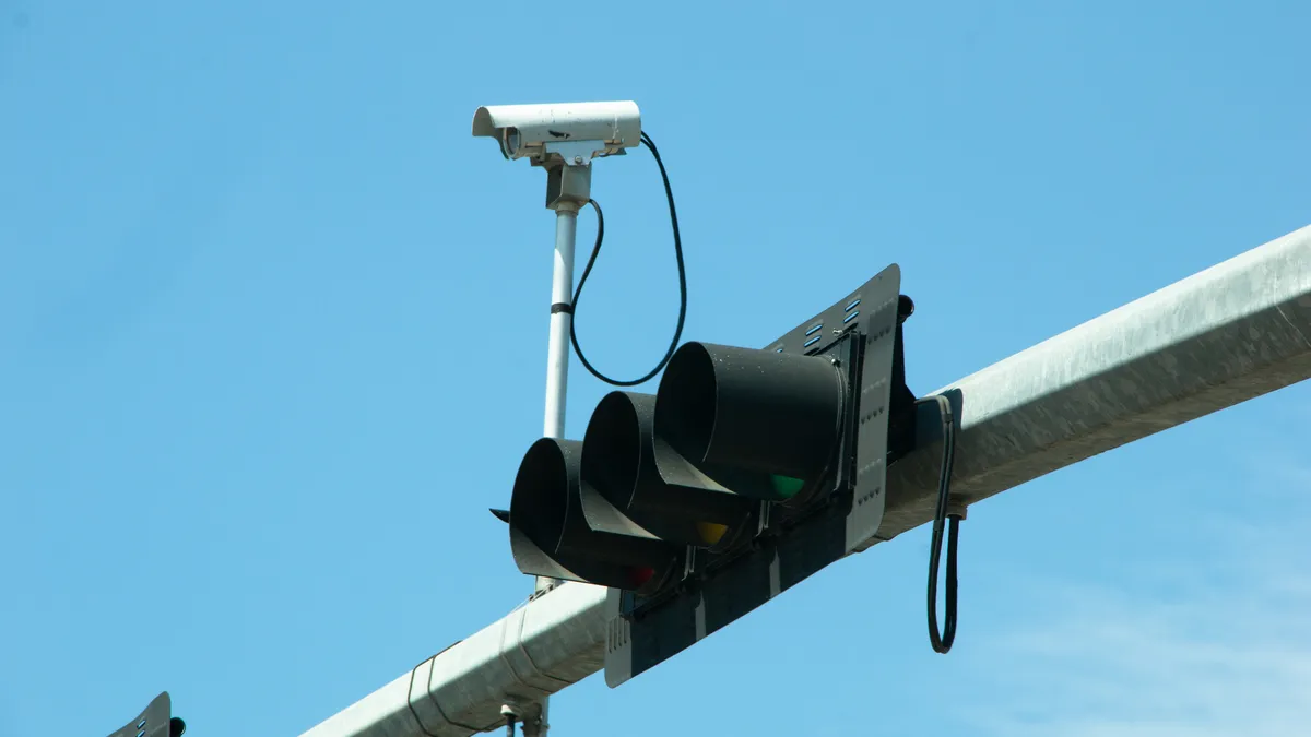 A traffic signal mounted horizontally on an overhead arm next to a camera.