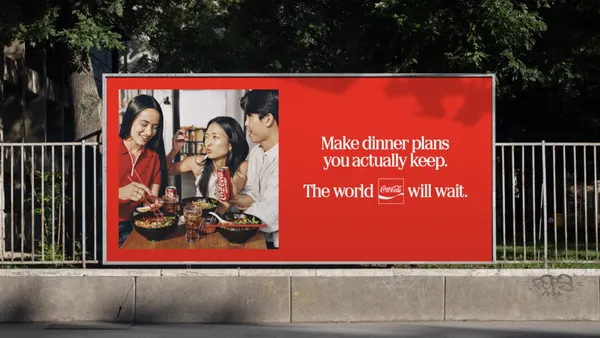 An outdoor billboard for Coke shows a group of people enjoying a meal