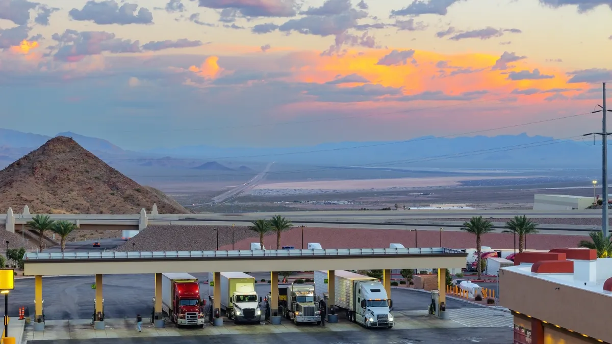 Trucks fueling against a dramatic evening sky showing sunlight across clouds amid a desert landscape.