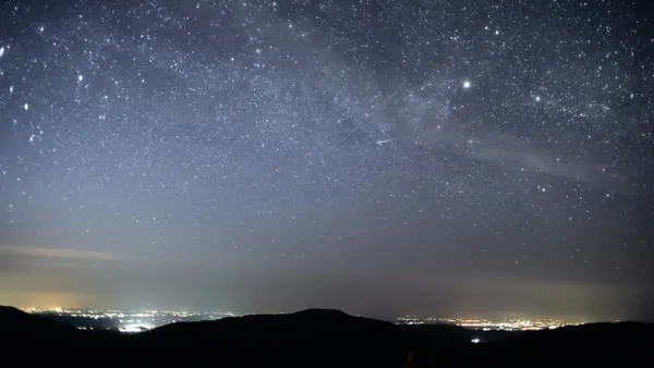 Silhouette of hills and light emanating from faraway buildings under starry night sky