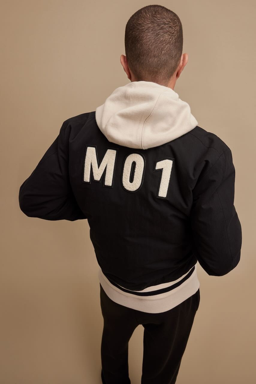 A person wearing a dark jacket and white hoodie, seen from the back.