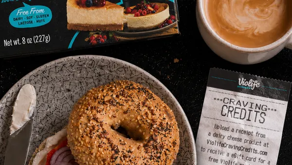 A bagel sits on a plate near a box of Violife cream cheese spread, a coffee and a receipt.