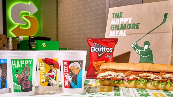 A row of four cups with illustrations of "Happy Gilmore 2" characters are lined up next to a Subway sandwich.