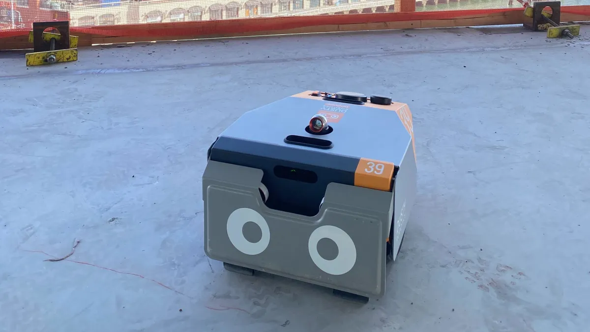 The grey, nearly rectangular FieldPrinter robot rests on a concrete floor with a cityscape in the background.