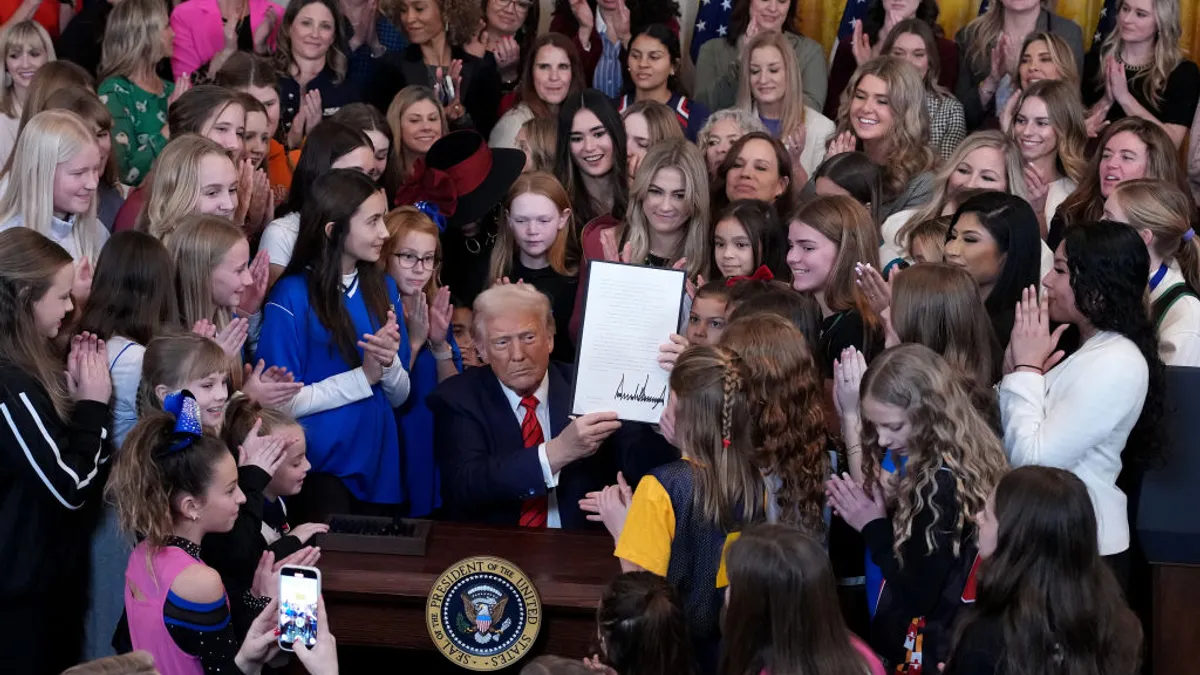 Trump holds up his signed executive order while surrounded by girl and women athletes.