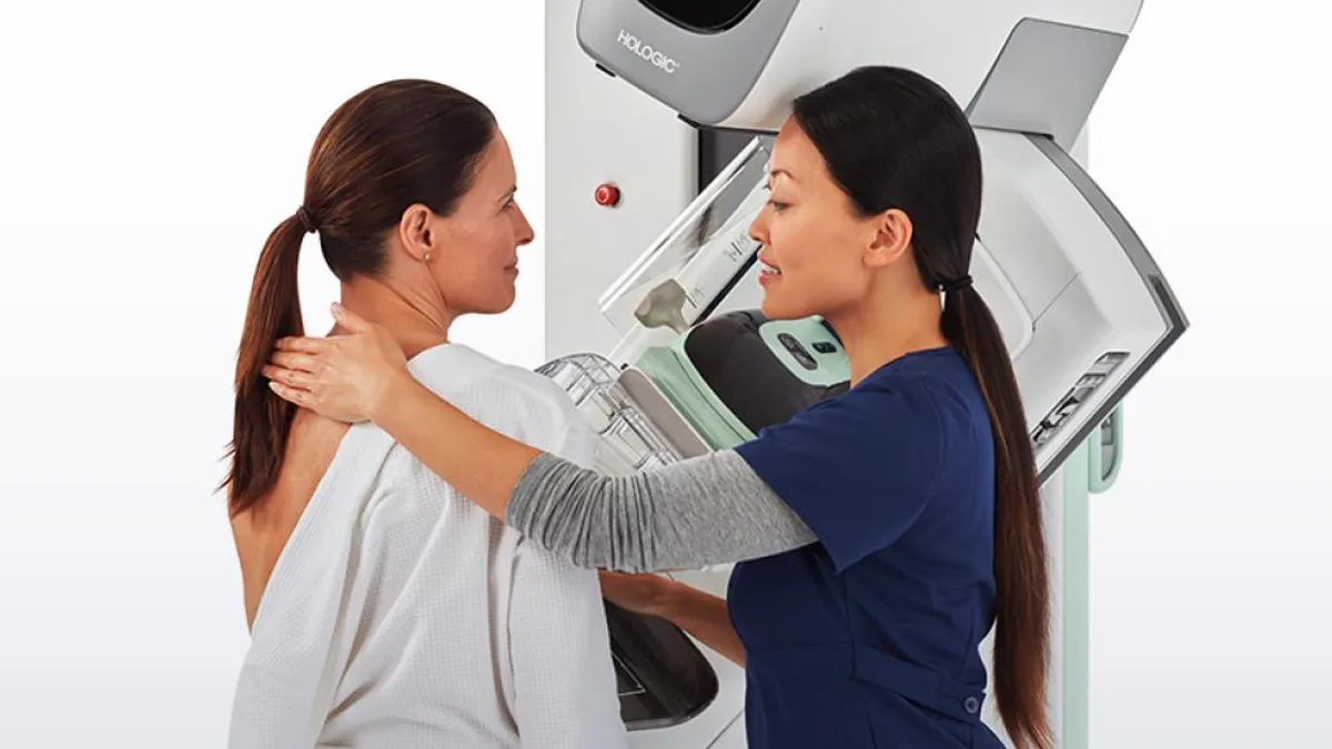 A patient and clinician in front of a Hologic breast imaging device