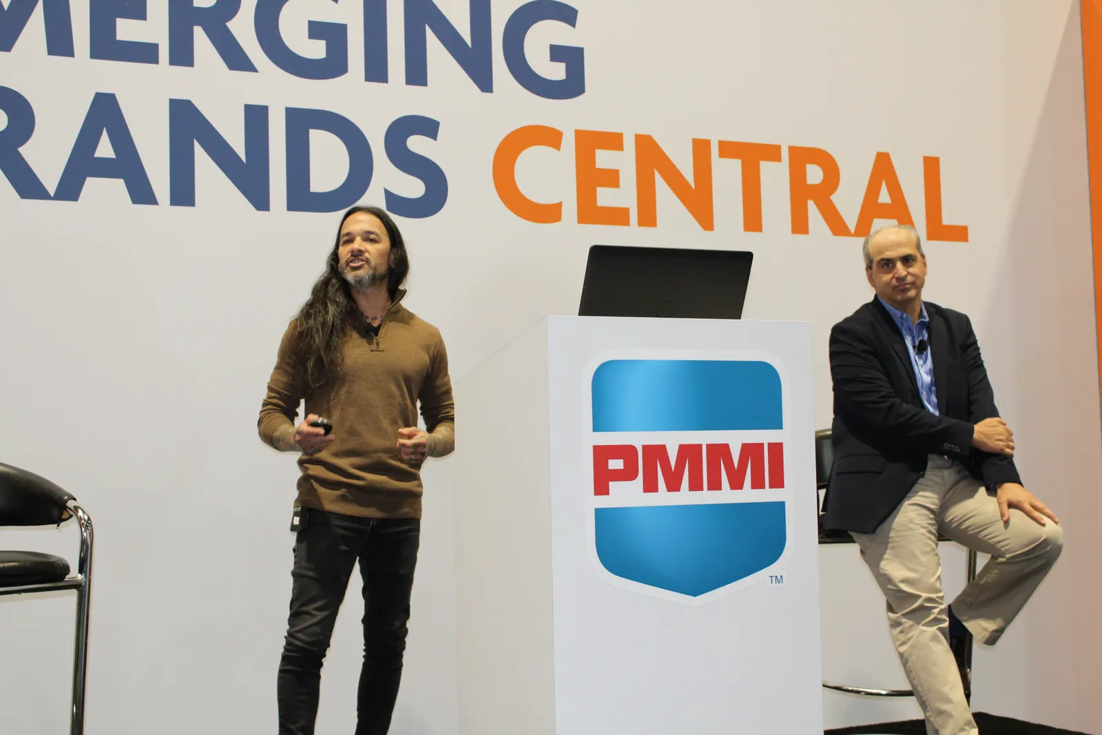 Two people on a conference stage speak to an audience.