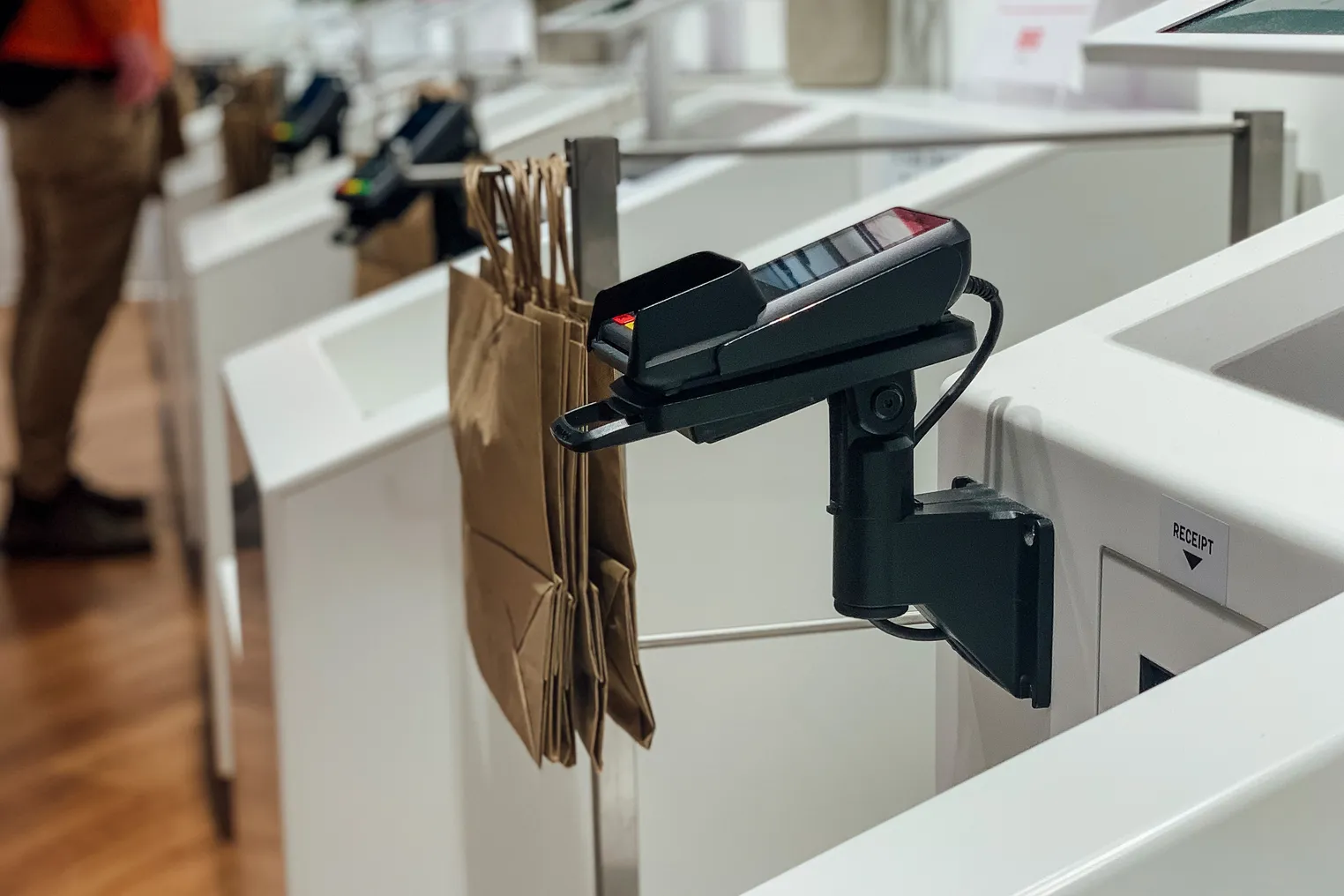 A close up of a payment terminal next to a white self checkout bin with paper bags hanging.