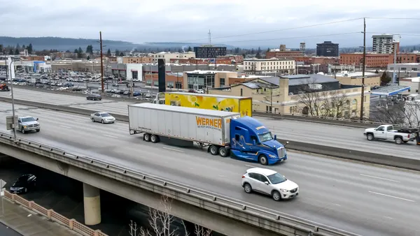 A Werner Enterprises tractor-trailer traveling through the downtown city center of Spokane, Washington, on a highway with passenger and commercial traffic nearby.