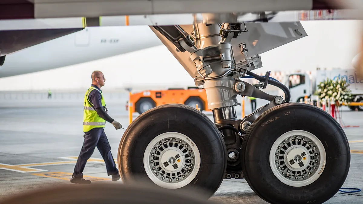 Landing gear (wheels) of Boeing's 787-8 Dreamliner on a runway as a person in a yellow vest walks past.