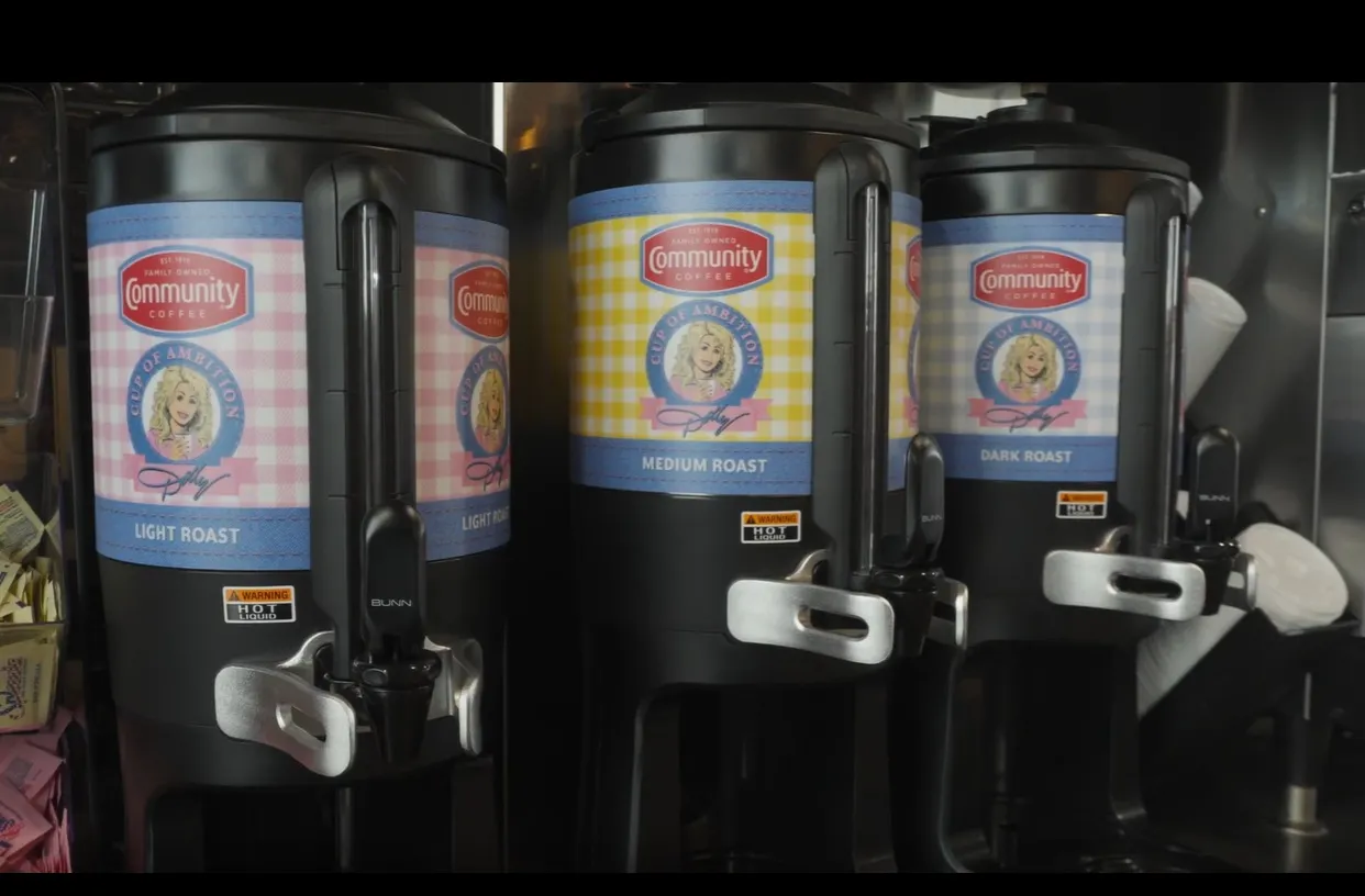 Three coffee containers with spigots. A logo on th side of each shows Dolly Parton's face, the Community Coffee logo and the words light roast, medium roast and dark roast.