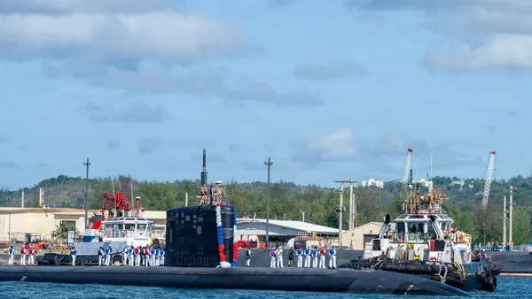 A submarine sails through a harbor on a sunny day.
