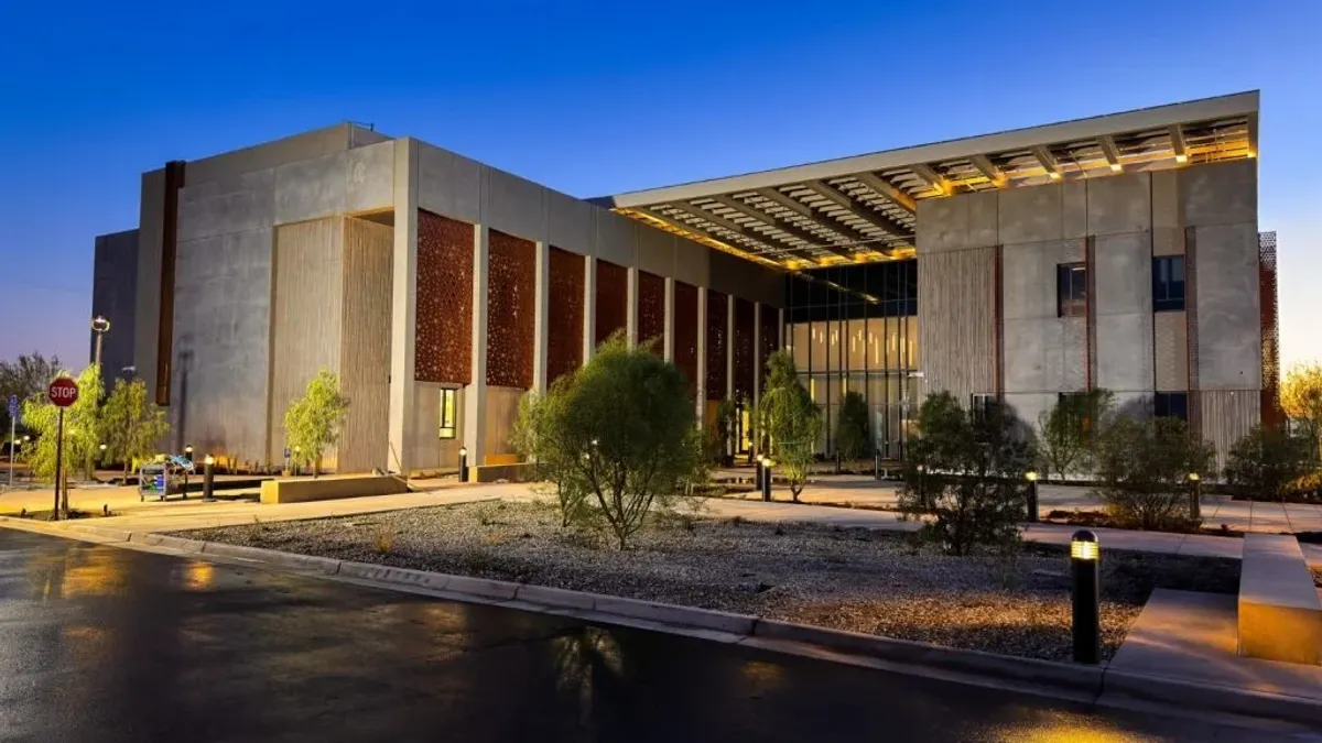 A building at night lit up by lights up front. It is large, brown and blocky.