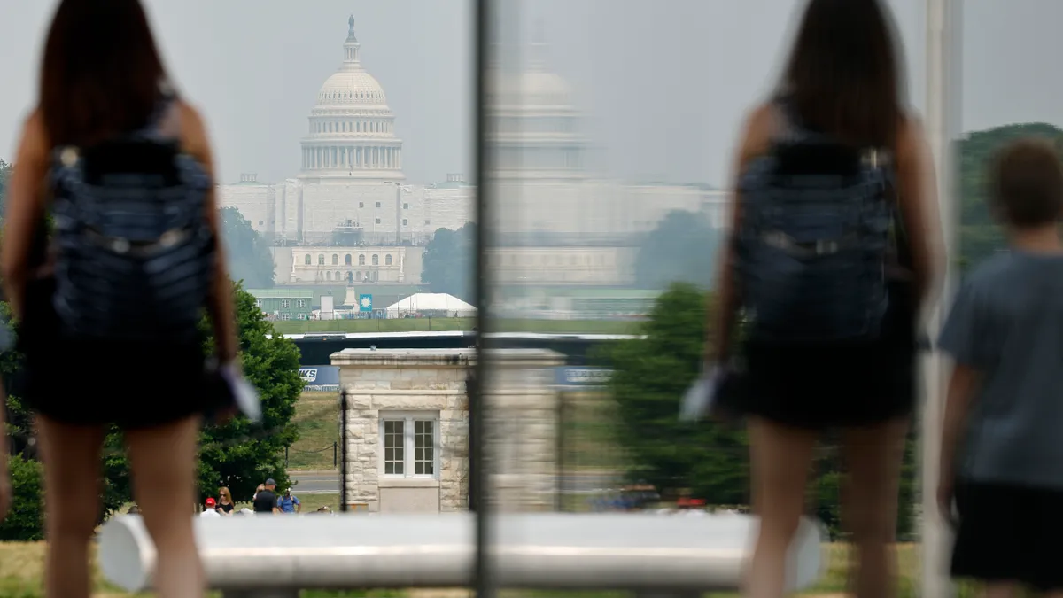 A tourist stands on the National Mall with the U.S. Capitol in the distance.