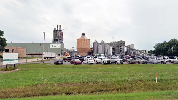An exterior view of an industrial facility with cars in an adjacent parking lot.