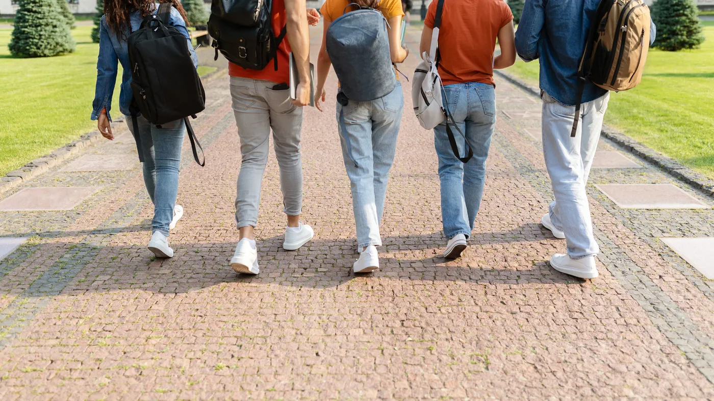 A group of five college students walk outside on a pathway.