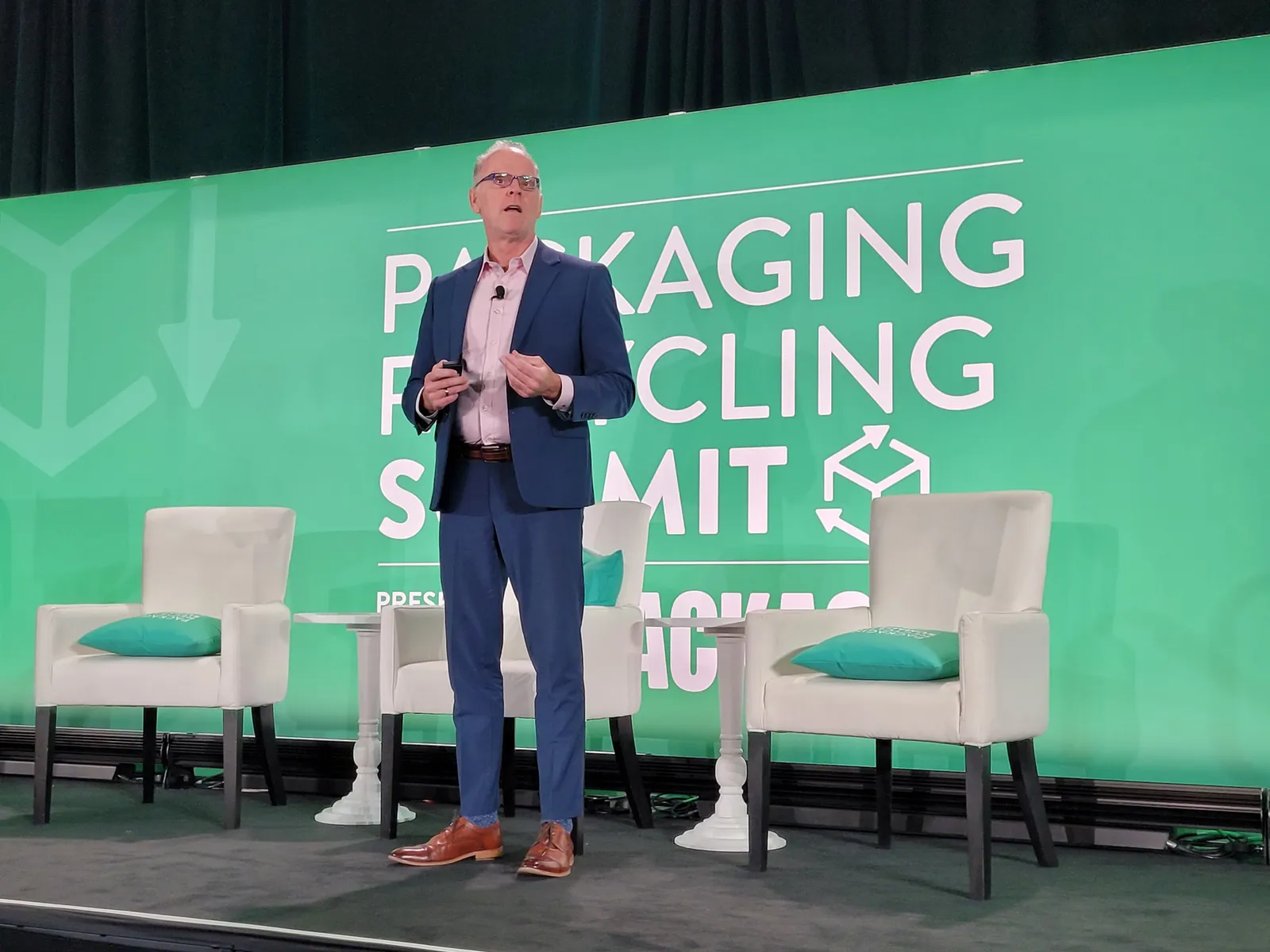 A person speaks on a stage in front of a green background that says Packaging Recycling Summit.