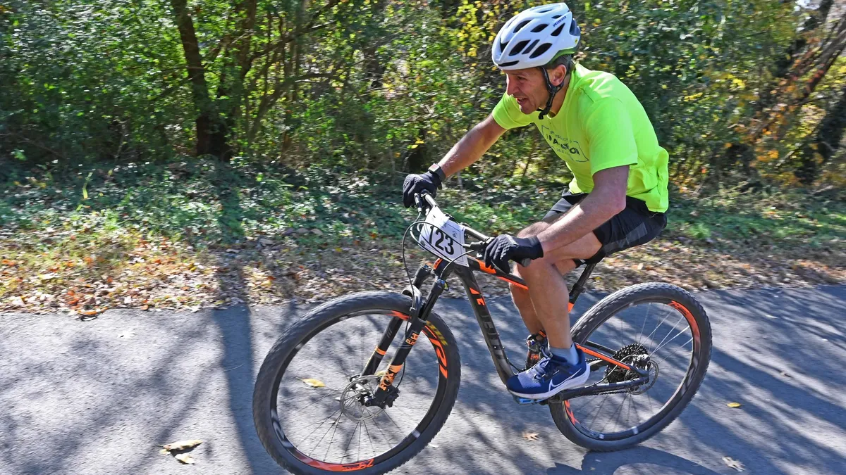 Man wearing a helmet riding a bicycle on a trail in the woods.