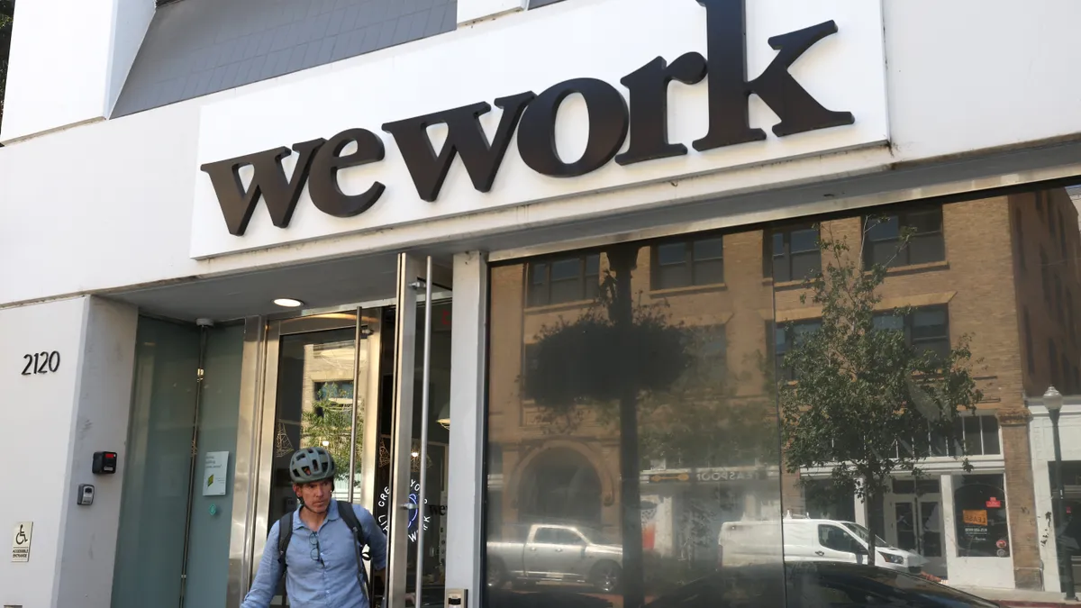 A person exits a building with a WeWork plaque on the exterior