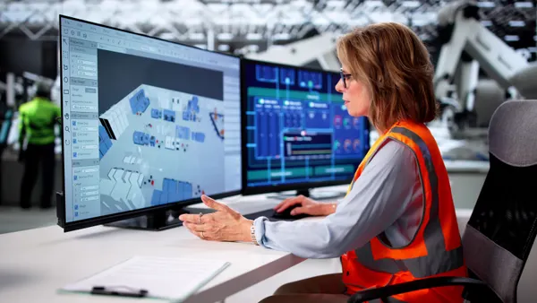 A construction worker at a desk with multiple computer monitors.