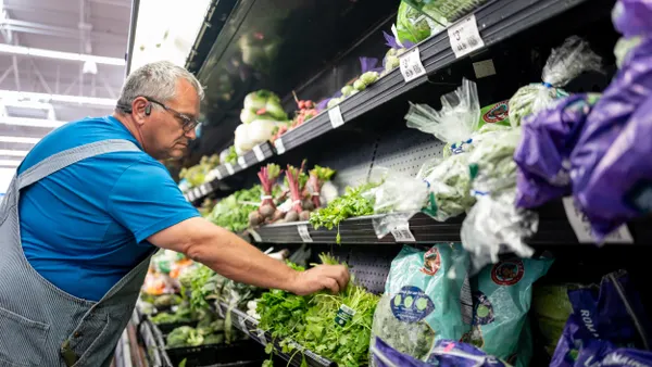 A person wearing a blue shirt reaches for cilantro in a grocery produce section.
