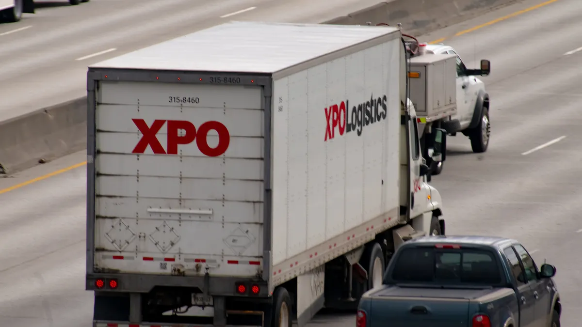 An XPO tractor-trailer driving on an urban section of interstate freeway in Spokane, Washington, alongside pickup trucks.