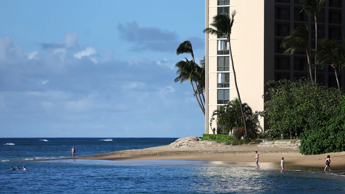 Visitors walk along a beach by a hotel.