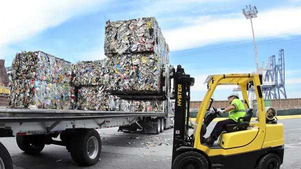 A Recology worker drives a forklift next to a truck carrying bales of recyclables