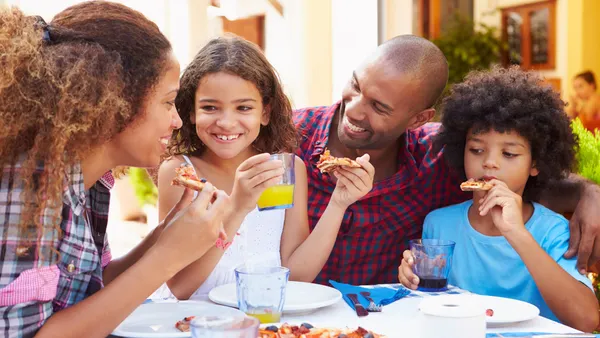 Two adults with two kids eats pizza at a restaurant.