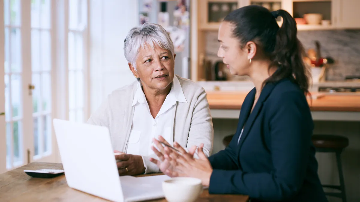 An older woman uses a laptop with a younger colleague in a coworking space