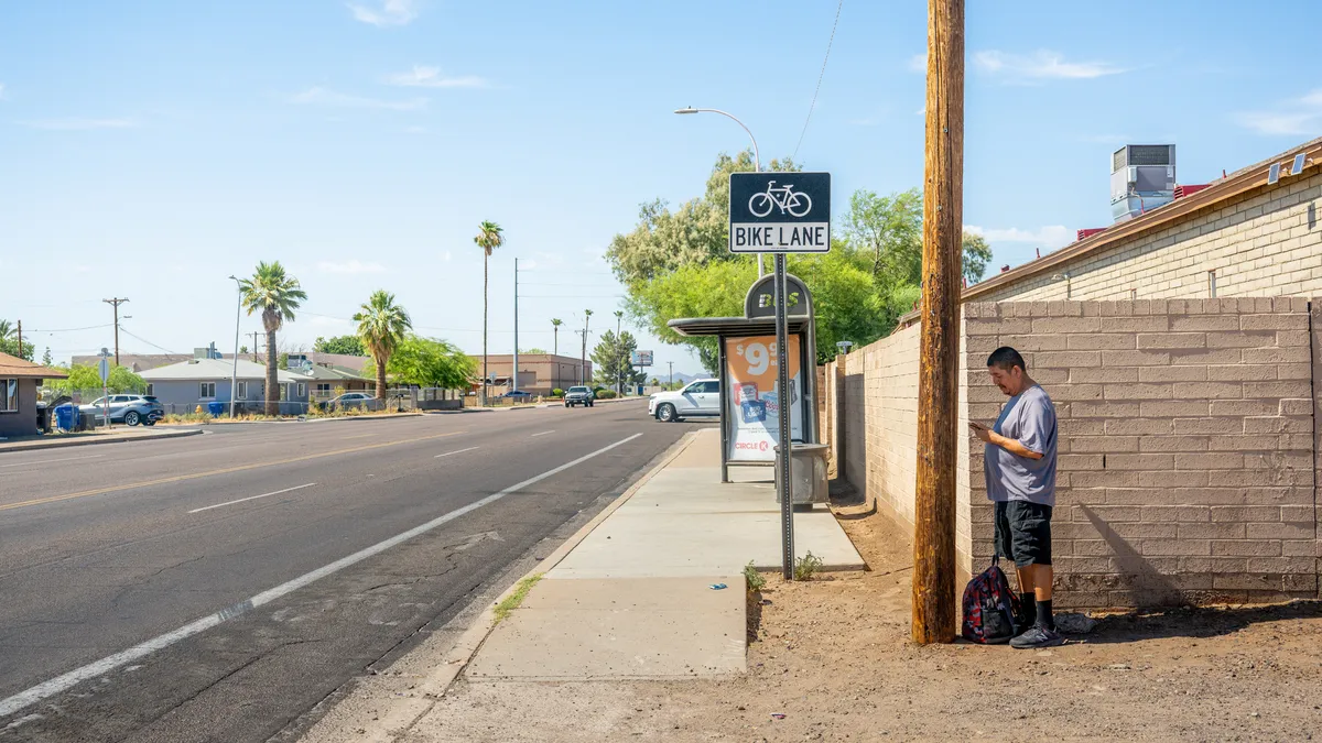 A person stands in the shade of a pole on the side of the road