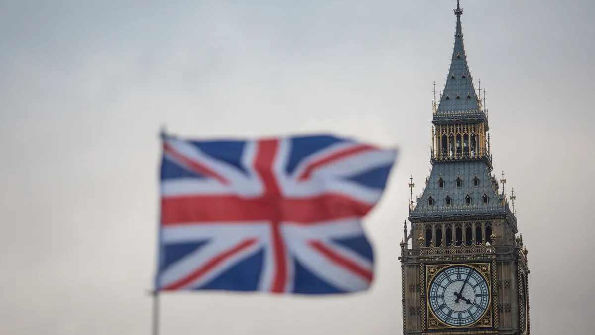 The flag of the UK flies in cloudy skies, the Big Ben featured in the foreground.