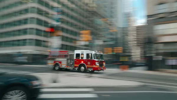 A red fire engine speeds through a city street with tall buildings in the background.