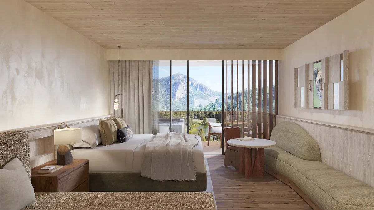 A beige-colored hotel room with a view of the mountains through the window.