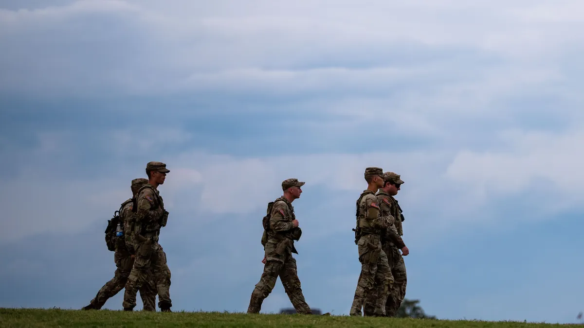 Five people wearing military fatigues walking with blue sky overhead.