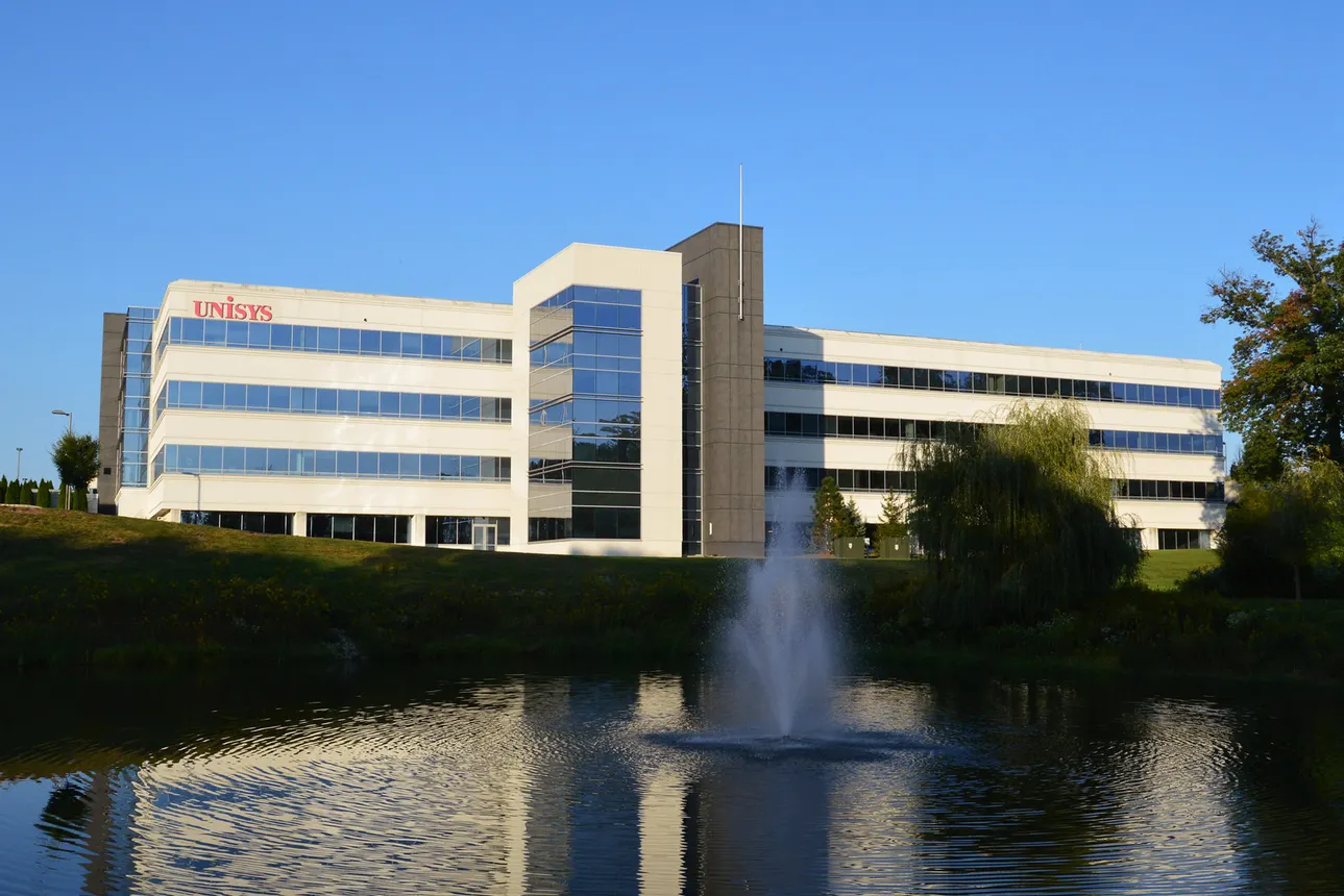 The Unysis logo is adhered to the top left side facade of a corporate building, and a pond with a water feature is in the foreground.