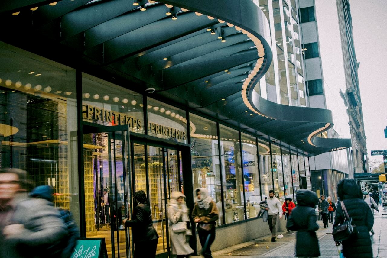 People mill around the entrance of a store with a wavy overhang.