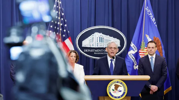 Three officials stand behind a podium at the Department of Justice.