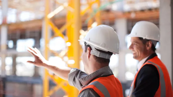 Two people in hardhats look out from a high view into an in-progress building.