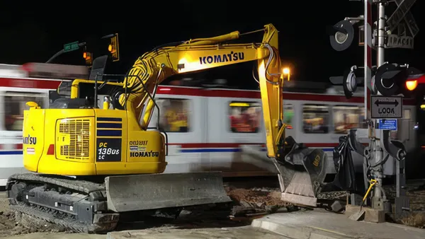A backhoe at a construction site with a train passing behind.