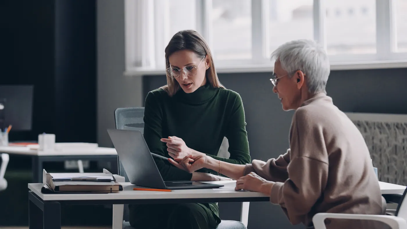 an older worker speaks with a younger worker during a meeting